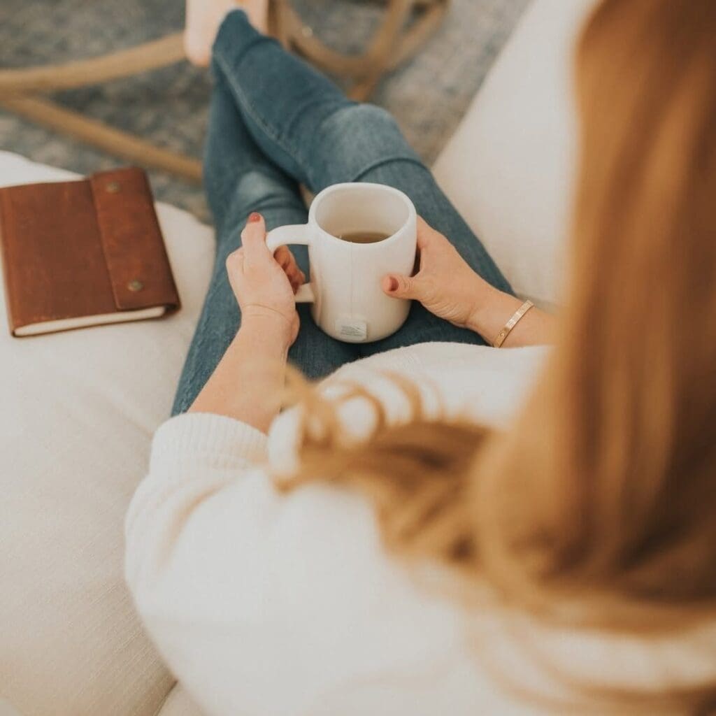 Woman sitting on couch with coffee in hand and journal next to her